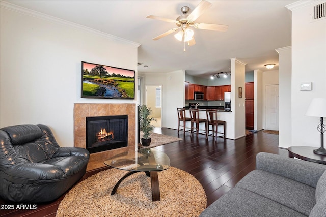 living room with crown molding, ceiling fan, track lighting, a tile fireplace, and dark hardwood / wood-style floors