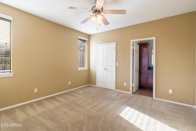 unfurnished bedroom with ceiling fan, multiple windows, carpet flooring, ensuite bath, and a closet