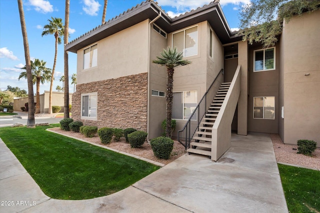 view of property exterior featuring a tile roof, a yard, stucco siding, stone siding, and stairs