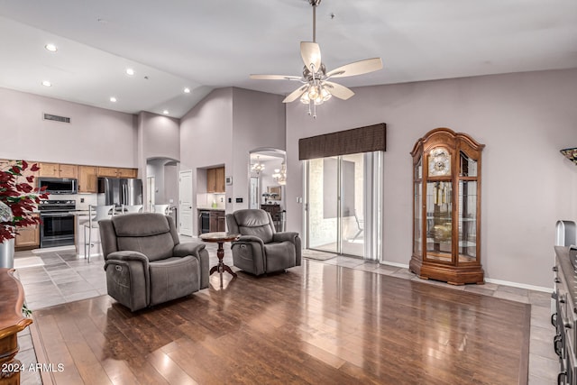 living room featuring ceiling fan with notable chandelier, light wood-type flooring, and high vaulted ceiling