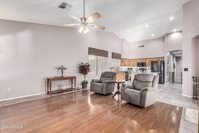 living room featuring ceiling fan, sink, high vaulted ceiling, and light wood-type flooring