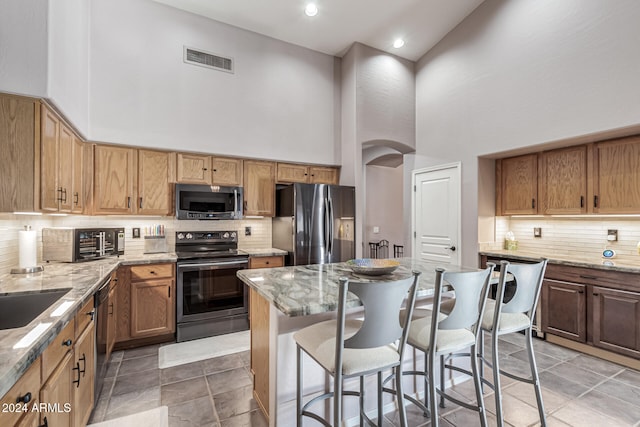 kitchen with a kitchen bar, light stone counters, a high ceiling, and appliances with stainless steel finishes