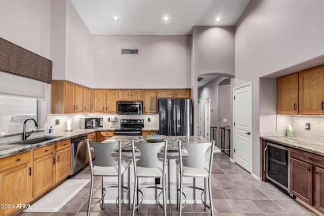 kitchen featuring sink, a high ceiling, wine cooler, a kitchen island, and appliances with stainless steel finishes