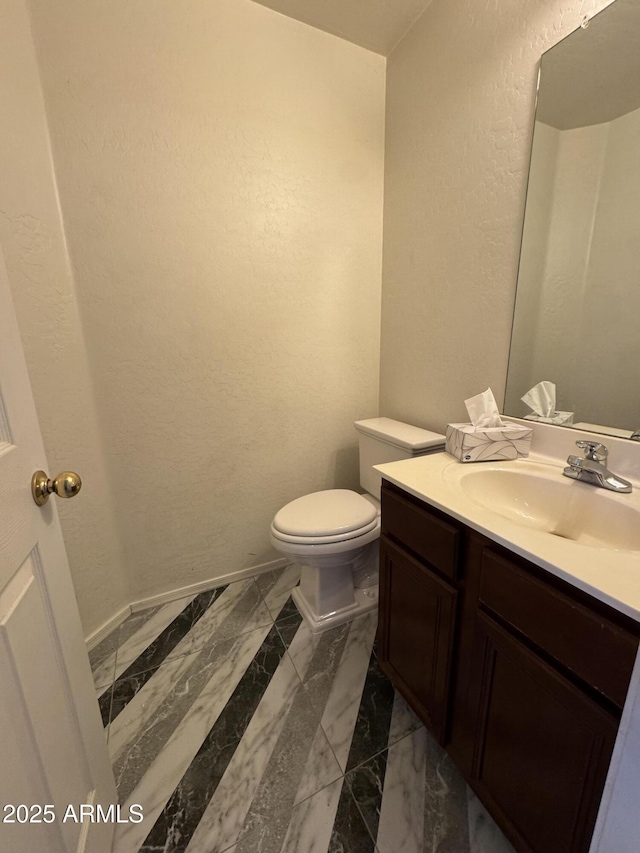 half bath with vanity, baseboards, a textured wall, toilet, and marble finish floor