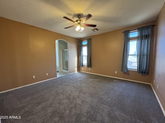 unfurnished room with carpet flooring, a textured ceiling, a ceiling fan, visible vents, and arched walkways