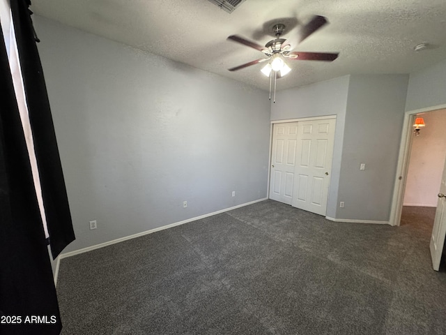 unfurnished bedroom with a closet, baseboards, dark carpet, ceiling fan, and a textured ceiling