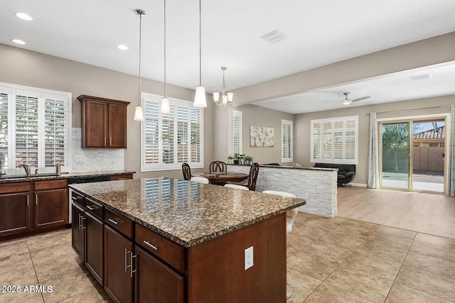 kitchen with ceiling fan with notable chandelier, a center island, dark stone counters, sink, and backsplash