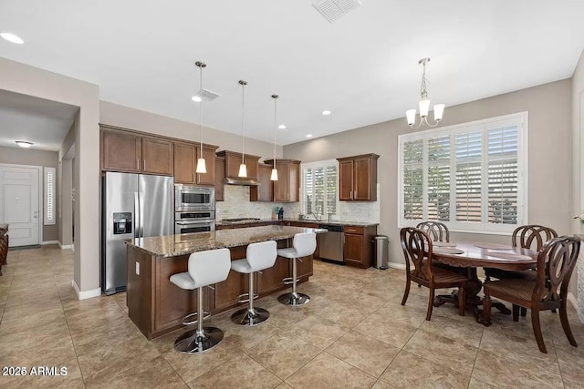 kitchen featuring premium range hood, appliances with stainless steel finishes, dark stone counters, pendant lighting, and a center island