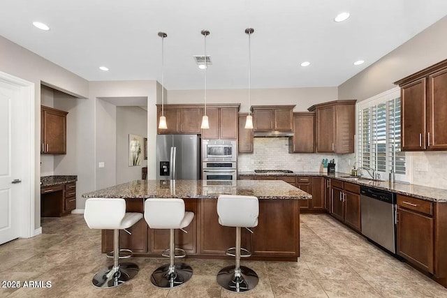 kitchen featuring dark stone counters, appliances with stainless steel finishes, a kitchen island, and decorative light fixtures