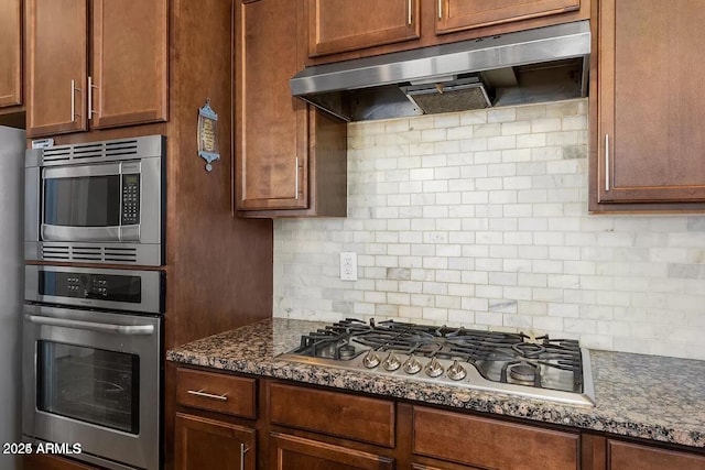 kitchen featuring appliances with stainless steel finishes, dark stone countertops, and backsplash