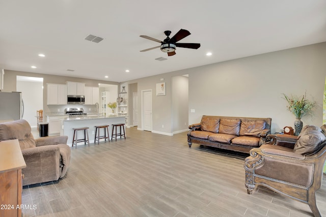 living room featuring light wood-type flooring, ceiling fan, and sink