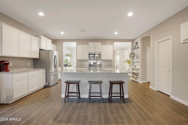 kitchen with a center island with sink, dark hardwood / wood-style floors, appliances with stainless steel finishes, light stone counters, and white cabinetry