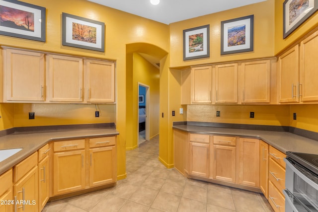 kitchen with stainless steel electric stove, light tile patterned flooring, and light brown cabinetry