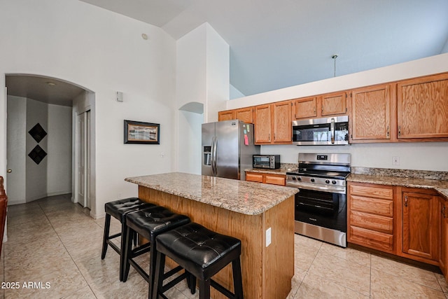 kitchen with a kitchen island, a breakfast bar, light stone counters, appliances with stainless steel finishes, and arched walkways