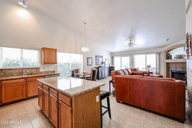 kitchen featuring brown cabinetry, a fireplace, a sink, a kitchen bar, and a center island