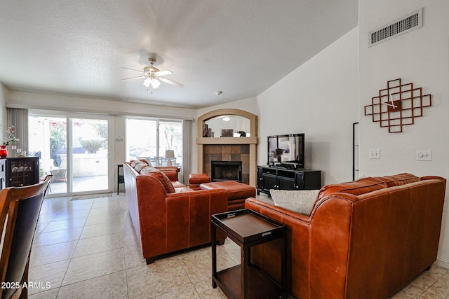 living room featuring light tile patterned floors, visible vents, a fireplace, ceiling fan, and vaulted ceiling