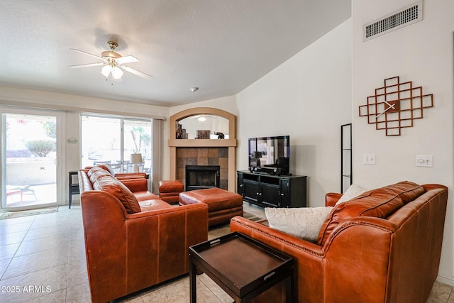 living room with light tile patterned floors, visible vents, lofted ceiling, ceiling fan, and a tiled fireplace