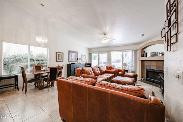 living room with light tile patterned floors, lofted ceiling, a fireplace, and ceiling fan with notable chandelier