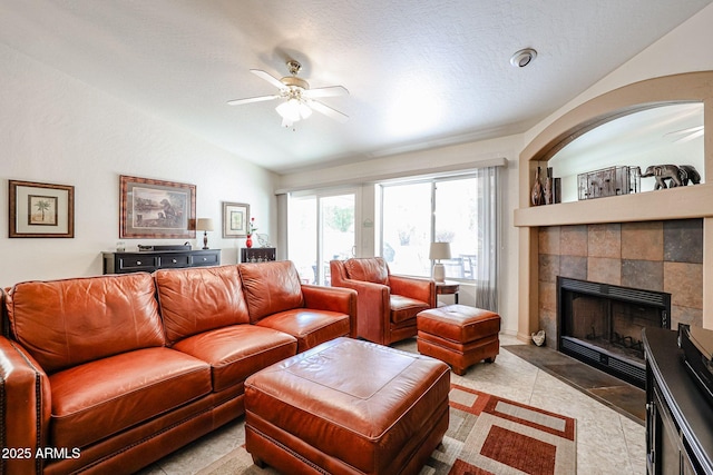 living room featuring vaulted ceiling, light tile patterned floors, a tile fireplace, a textured ceiling, and a ceiling fan