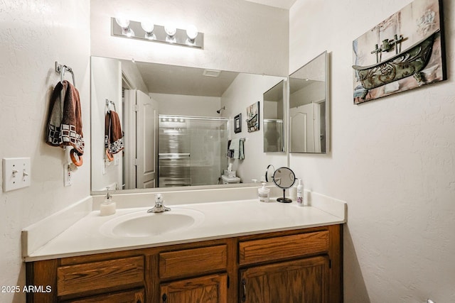 bathroom with vanity, an enclosed shower, and a textured wall