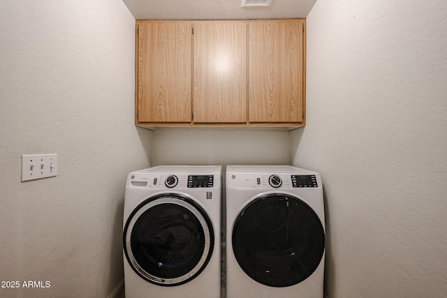 laundry area with visible vents, cabinet space, a textured wall, and separate washer and dryer