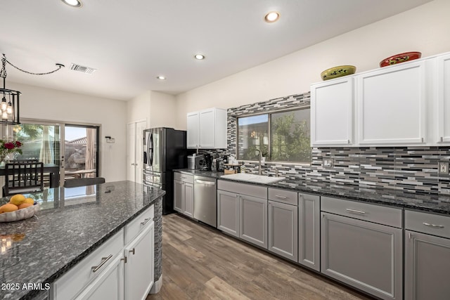 kitchen with white cabinetry, sink, stainless steel appliances, dark stone counters, and decorative light fixtures