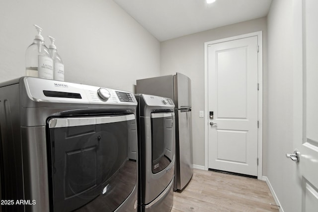 washroom featuring laundry area, light wood-style flooring, washing machine and dryer, and baseboards