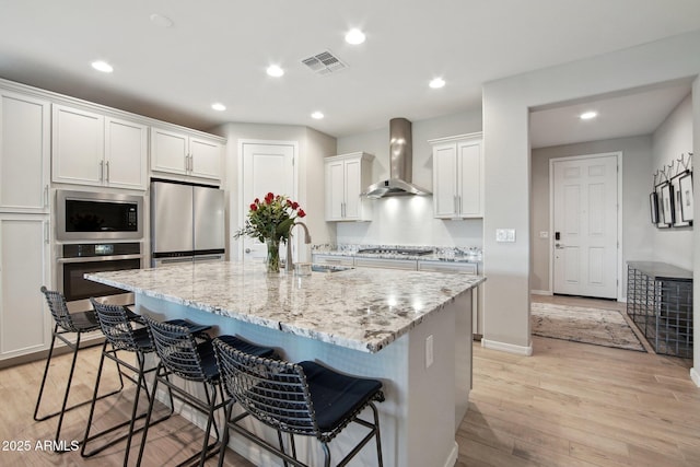 kitchen with visible vents, light wood finished floors, a sink, appliances with stainless steel finishes, and wall chimney exhaust hood