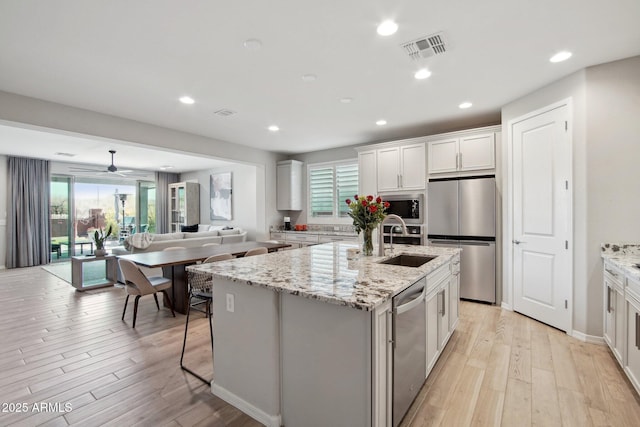 kitchen featuring visible vents, a kitchen island with sink, a sink, stainless steel appliances, and light wood-style floors