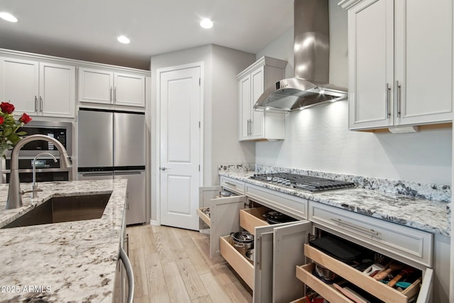 kitchen featuring light wood-style flooring, a sink, white cabinetry, appliances with stainless steel finishes, and wall chimney exhaust hood