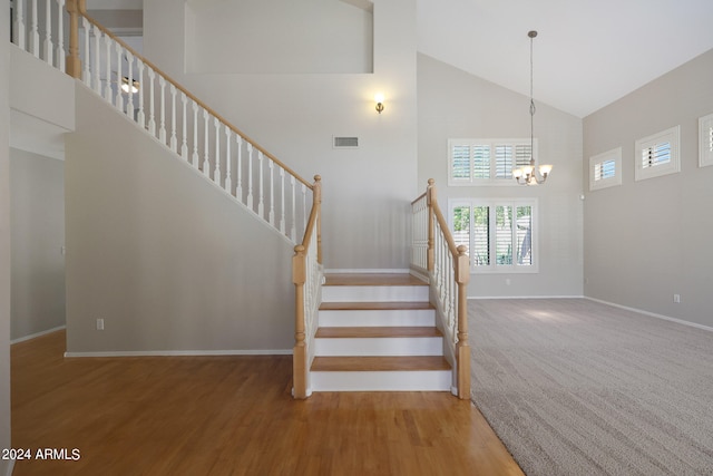 stairway featuring hardwood / wood-style flooring, a chandelier, and high vaulted ceiling