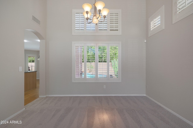 carpeted spare room with a high ceiling and a chandelier