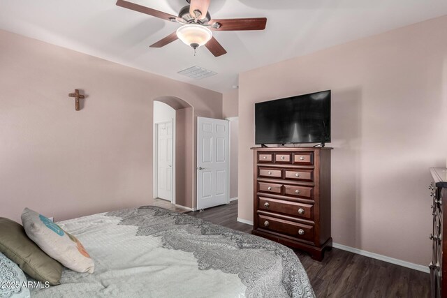 bedroom with baseboards, dark wood-style floors, visible vents, ceiling fan, and arched walkways