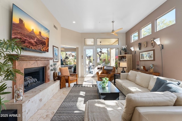 living room featuring a ceiling fan, a towering ceiling, a premium fireplace, and visible vents