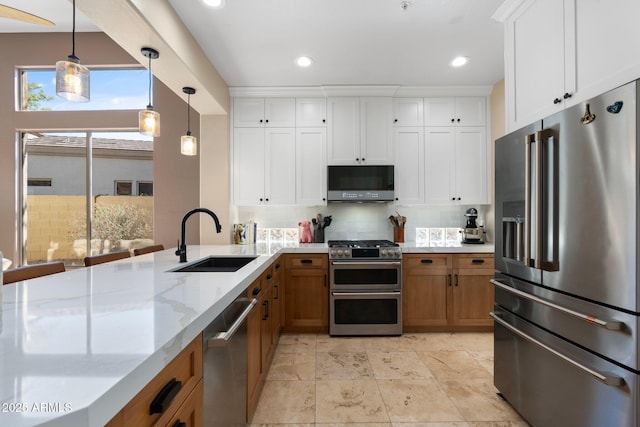 kitchen featuring light stone countertops, brown cabinets, stainless steel appliances, a sink, and pendant lighting
