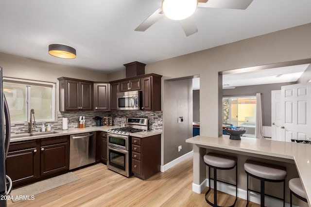 kitchen with appliances with stainless steel finishes, light wood-type flooring, tasteful backsplash, dark brown cabinetry, and sink