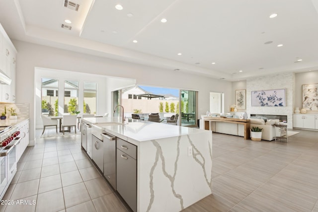 kitchen with white cabinetry, a large island, light stone counters, and a tray ceiling