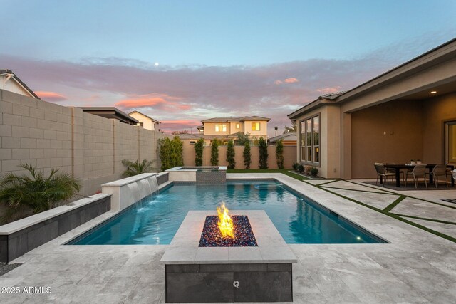 pool at dusk featuring pool water feature, a patio area, and a fire pit