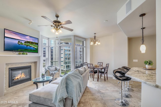 living room featuring ceiling fan with notable chandelier, baseboards, a glass covered fireplace, and visible vents