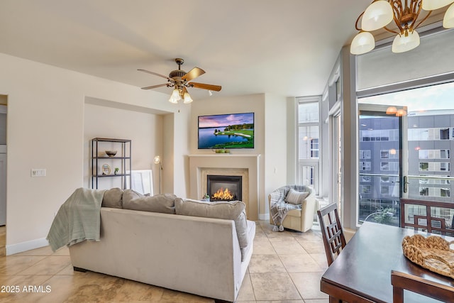 living area with a ceiling fan, baseboards, a glass covered fireplace, and light tile patterned floors