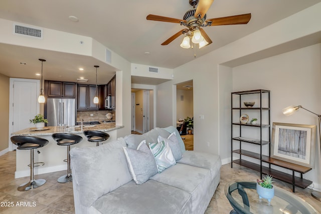 living area featuring light tile patterned floors, visible vents, baseboards, and a ceiling fan