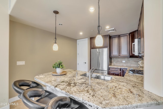 kitchen with a sink, pendant lighting, visible vents, appliances with stainless steel finishes, and light stone counters
