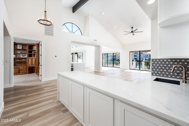 kitchen with ceiling fan with notable chandelier, light stone countertops, pendant lighting, white cabinets, and sink