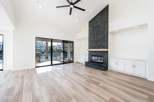 unfurnished living room with high vaulted ceiling, ceiling fan, a fireplace, and light wood-type flooring