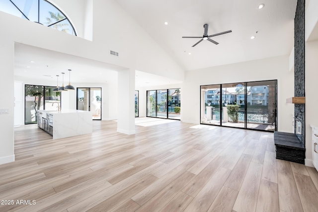 unfurnished living room with ceiling fan, a towering ceiling, sink, and light hardwood / wood-style floors