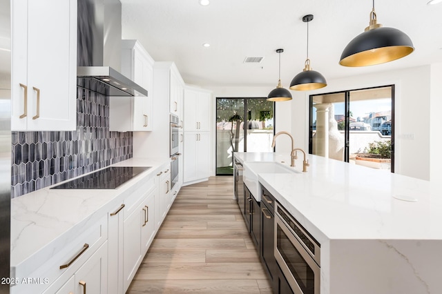 kitchen with a spacious island, wall chimney exhaust hood, stainless steel appliances, tasteful backsplash, and hanging light fixtures