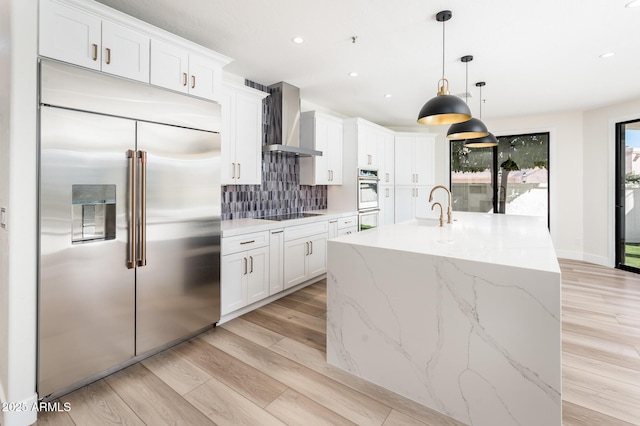 kitchen with pendant lighting, white cabinets, wall chimney range hood, stainless steel appliances, and backsplash