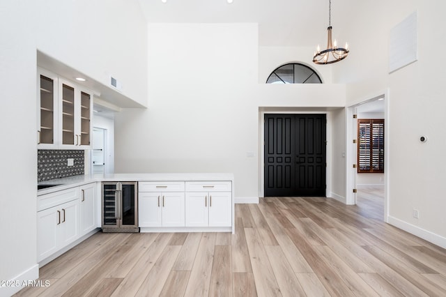 bar with decorative backsplash, a towering ceiling, wine cooler, pendant lighting, and white cabinets