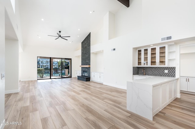 unfurnished living room featuring ceiling fan, a fireplace, light hardwood / wood-style floors, beam ceiling, and high vaulted ceiling