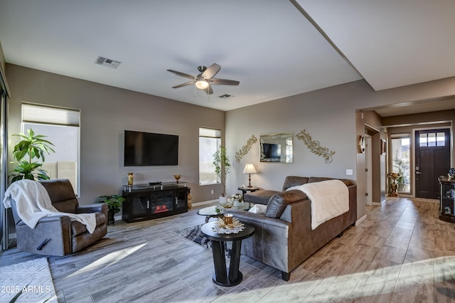 living room featuring ceiling fan, plenty of natural light, and a fireplace